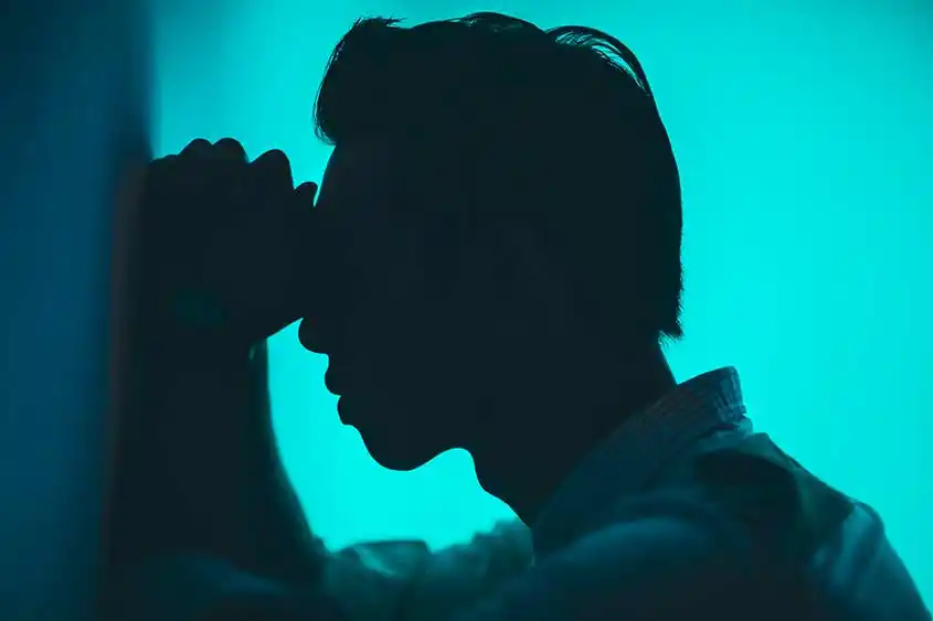 Silhouette of young man with head against closed fists, possibly undergoing depression