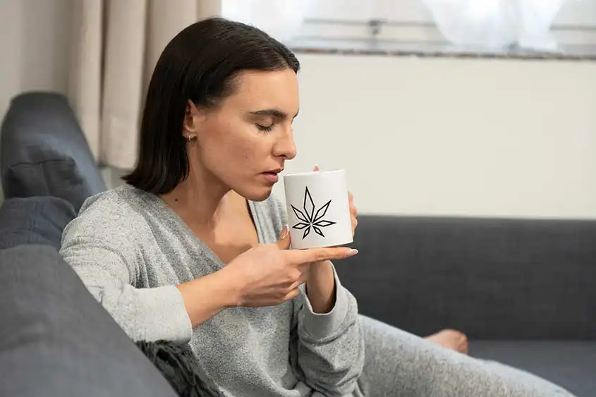 Woman drinking from a cup with a cannabis print on it, looking relaxed and peaceful. We are guessing she's enjoying some medical marijuana infused beverage!