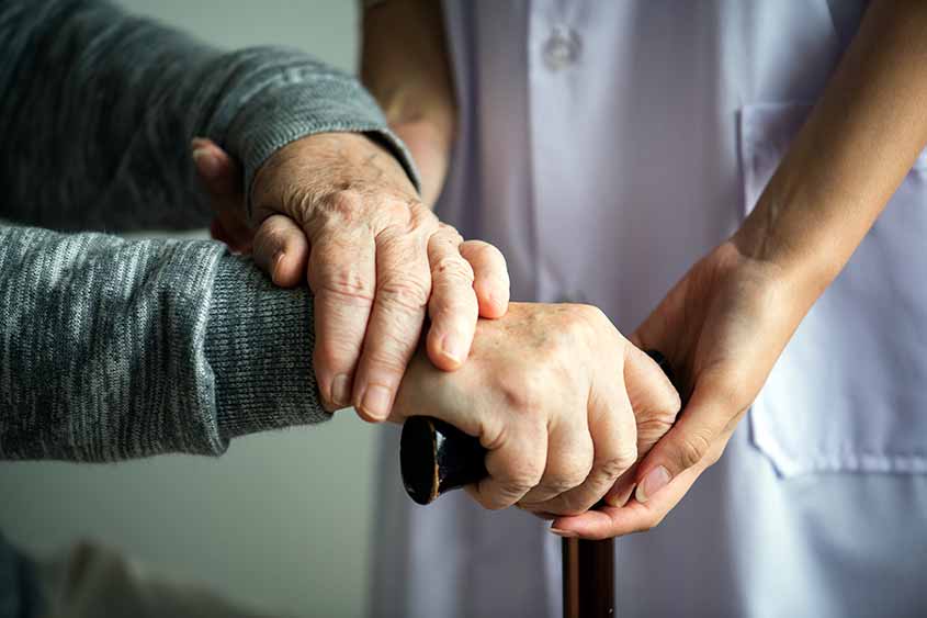 Close up of a movement impaired person holding a walking stick, with help