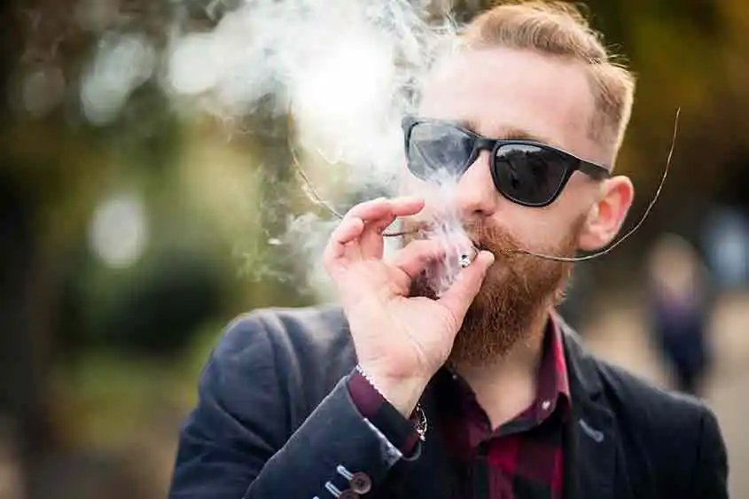 Man in dark glasses vaping with a vaporizer in the outdoors