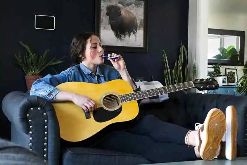 Young woman with a guitar using a vape